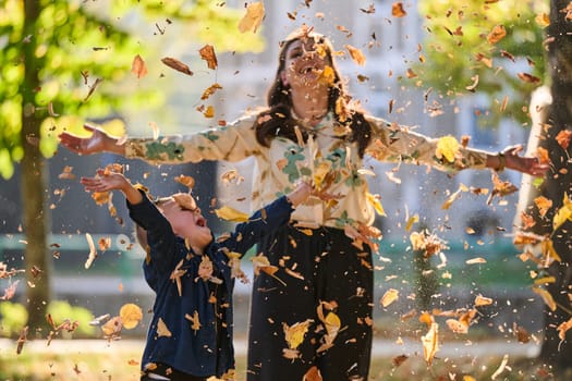 A modern woman joyfully plays with her son in the park, tossing leaves on a beautiful autumn day, capturing the essence of family life and the warmth of mother-son bonding in the midst of the fall season.