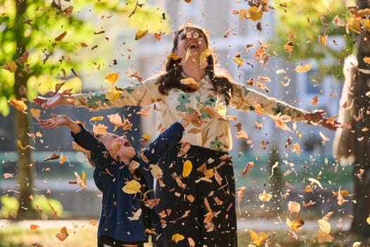 A modern woman joyfully plays with her son in the park, tossing leaves on a beautiful autumn day, capturing the essence of family life and the warmth of mother-son bonding in the midst of the fall season.