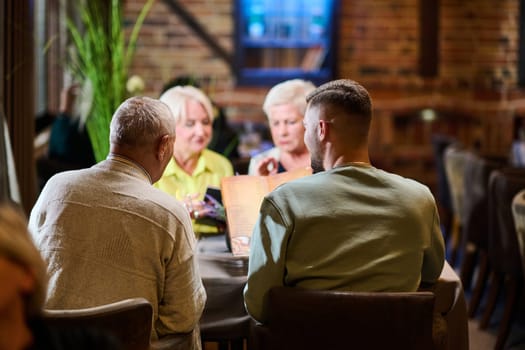 A group of family friends, comprising a young grandson and older individuals, share a delightful dinner in a modern restaurant, exemplifying the concept of healthy aging through intergenerational bonding and a joyous dining experience.