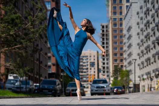 Beautiful Asian ballerina in blue dress posing in splits outdoors. Urban landscape