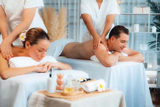 Caucasian couple customer enjoying relaxing anti-stress spa massage and pampering with beauty skin recreation leisure in day light ambient salon spa at luxury resort or hotel. Quiescent