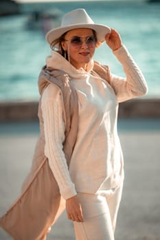 Happy blonde woman in a white suit and hat posing at the camera against the backdrop of the sea.