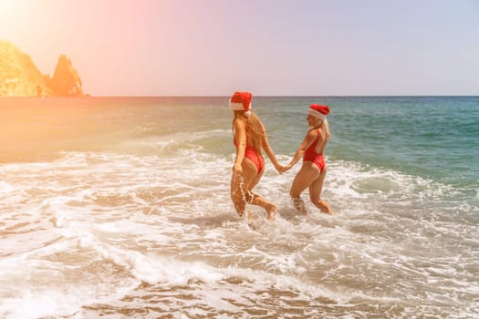 Women in Santa Claus hats run into the sea dressed in red swimsuits. Celebrating the New Year in a hot country.