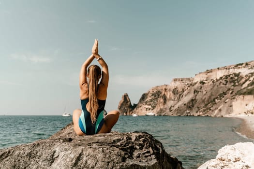 Yoga on the beach. A happy woman meditating in a yoga pose on the beach, surrounded by the ocean and rock mountains, promoting a healthy lifestyle outdoors in nature, and inspiring fitness concept