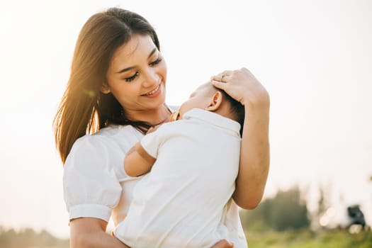 In a quiet park at dusk, a mother holds her sleeping baby, feeling warmth of setting sun. Her face is full of love and contentment as she takes in the beauty of garden. A perfect Mother's Day moment