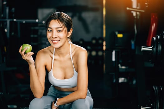 A fit and happy woman holding a green apple in a gym, emphasizing the benefits of including fresh fruit in a workout routine for a healthy lifestyle. Healthy fitness and eating lifestyle concept