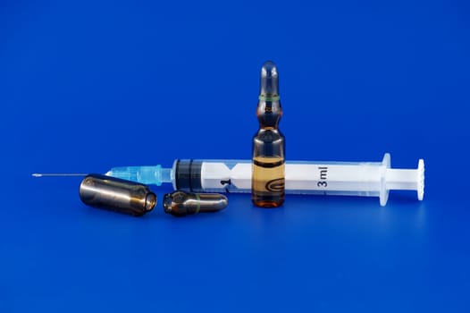 Needle, syringe and two brown vaccine ampules appearing ready for use against a blue background, medical treatment and vaccination