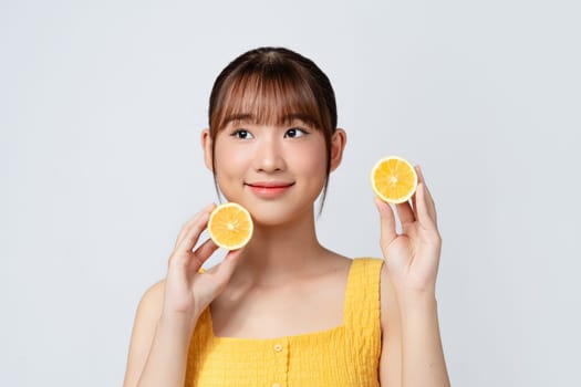 portrait of pretty young woman holding slices of orange, facial care