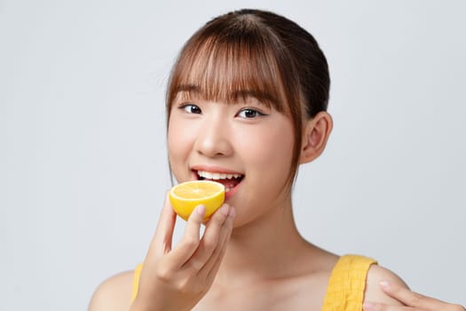 Beauty portrait of asian young woman smiling and eating lemon isolated over white background