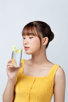 Beautiful young woman with healthy, well-kept skin taking care after health, drinking water with lemons