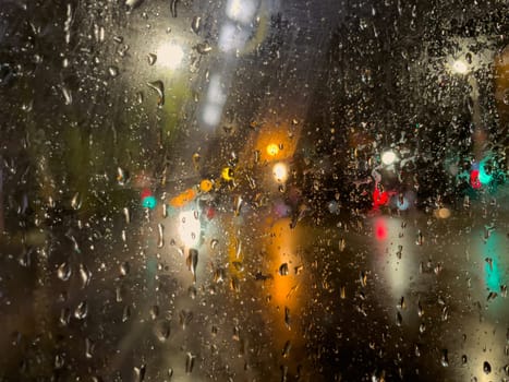 Rain bokeh road lights. Abstract shot of evening city traffic bokeh. Multicolored lights of the evening city and passing cars through a wet rainy window