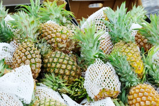 Ripe pineapples, encased in protective mesh, sits ready for purchase at a vibrant outdoor market.