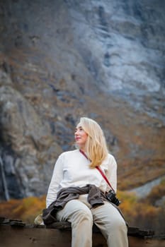 Force of Nature: A girl contemplates the majesty of a waterfall while sitting on a bridge in a mountain