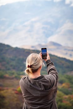Young woman taking pictures of beautiful mountains with camera, majesty of nature and photography
