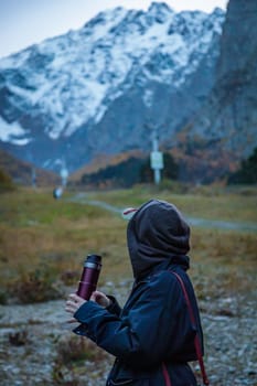 Solitude in the mountains: a girl enjoys coffee while looking at the majesty of a glacier