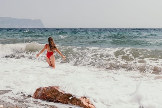 Woman travel sea. Young Happy woman in a long red dress posing on a beach near the sea on background of volcanic rocks, like in Iceland, sharing travel adventure journey