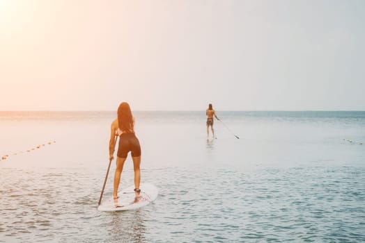 Sea woman and man on sup. Silhouette of happy young woman and man, surfing on SUP board, confident paddling through water surface. Idyllic sunset. Active lifestyle at sea or river