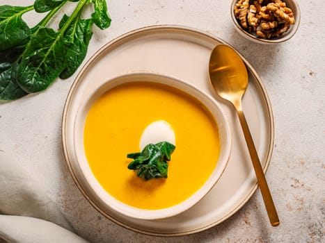 Pumpkin cream-soup served spinach, nuts, sour cream. Tasty Homemade Pumpkin, Sweet Potato or Carrot Soup in Bowl on Neutral Pastel Background. Cozy autumn comfort food. Top view