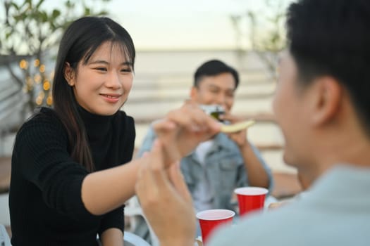 Cheerful young female and male friends enjoying dinner party at rooftop.