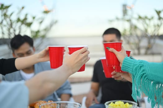 Young people celebrating friendship clinking plastic red cups at outdoor rooftop party.
