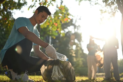 Young man volunteer picking bottles into plastic black bag for cleaning up nature. Environmental and ecology concept.