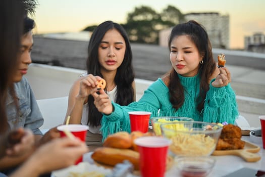 Young male and female friends enjoying dinner party at rooftop in evening.