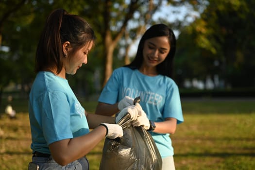 Two young female volunteers with garbage bag cleaning up the forest. Charity and ecology concept.