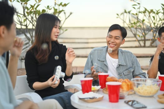 Group of young friends spending great time together chatting and drinking beer at rooftop party.