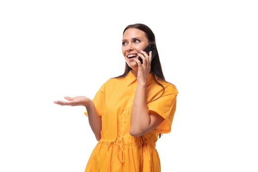 black-haired slender woman dressed in an orange dress speaks on the phone.