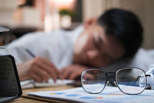 Exhausted businessman sleeping on his office desk, next to laptop and documents, tired of overworking.