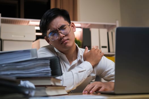 Asian businessman overtime work and feel shoulder pain in the office feeling tired, fatigue, exhausted while working overtime at night in office.
