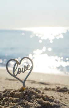 Plastic stick in shape of heart and word Love in sand on beach seashore on sunny summer day close-up. Figures in shape of heart word Love on background of sea waves. Love relationship romance concept