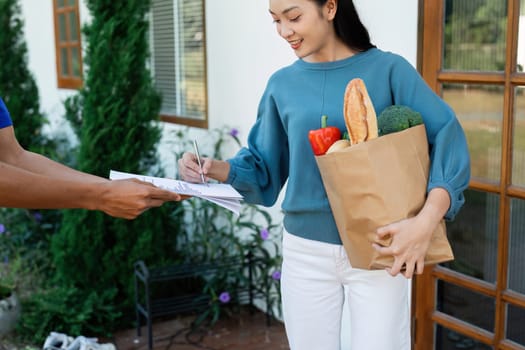 Asian woman signing the receipt on the order receipt through the online supermarket's home store.