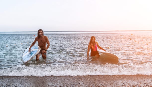 Sea woman and man on sup. Silhouette of happy young woman and man, surfing on SUP board, confident paddling through water surface. Idyllic sunset. Active lifestyle at sea or river