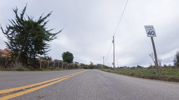 Vehicle navigates the streets of Morro Bay, California, during a cloudy winter day. The atmosphere is moody and serene as the overcast sky casts a soft light on the charming buildings and quiet streets of this coastal town.