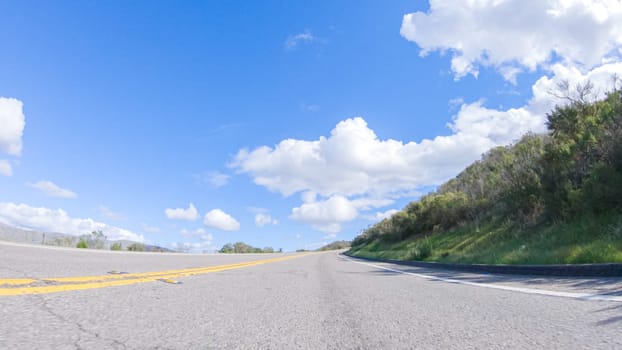 On a clear winter day, a car smoothly travels along Highway 101 near Santa Maria, California, under a brilliant blue sky, surrounded by a blend of greenery and golden hues.