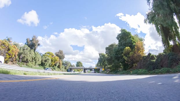 On a clear winter day, a car smoothly travels along Highway 101 near Santa Maria, California, under a brilliant blue sky, surrounded by a blend of greenery and golden hues.