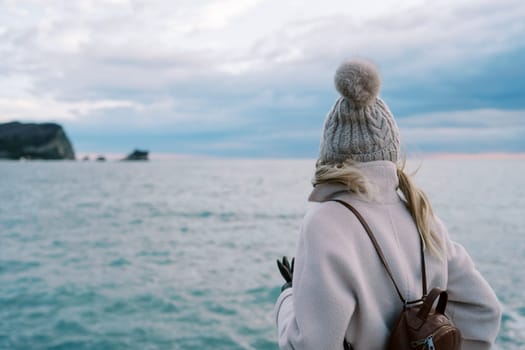 Girl with a backpack stands on the seashore and looks at the sunset. Back view. High quality photo