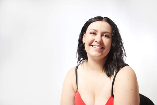 Portrait of attractive dreamy thick woman in red black swimsuit posing on white background. Body positive, photoshoot, selfie. Funny plus size model