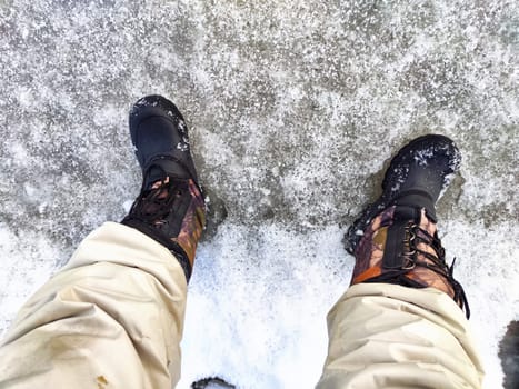 Feet of Hunter or fisherman in big warm boots on winter day on snow. Top view. Fisherman on the ice of a river, lake, reservoir on spring day with melting ice. Dangerous fishing in autumn