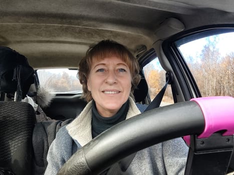 Portrait of female driver in solo journey. Adult mature woman holding steering wheel and looking through windscreen in travel by vehicle on vacation. Lady girl who is owner or rent car for travel