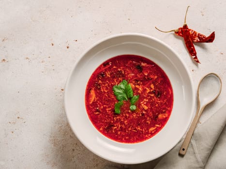 Traditional red soup borscht made with beetroot. National Russian and Ukrainian soup, kitchen, food. Tasty beetroot soup with greens in bowl on neutral pastel background. Top view, flat lay