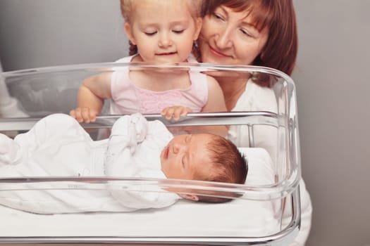 The sister and grandmother looks at a newborn baby in the hospital ward