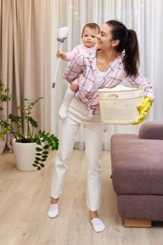 happy mother housewife is holding cute baby girl and basket with laundry at home, Happy family having fun