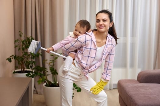 happy mother housewife is holding cute baby girl and doing housework at home, Happy family having fun