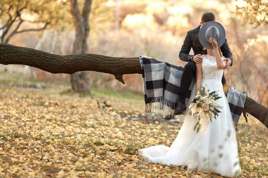 beautiful happy stylish bride and groom kissing and covering by hat outdoor in autumn