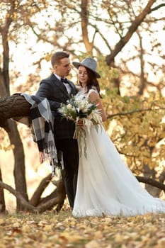 beautiful happy stylish bride in hat and groom standing outdoor in autumn