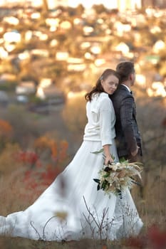 beautiful sensual bride in white wedding dress and groom standing outdoor on natural background