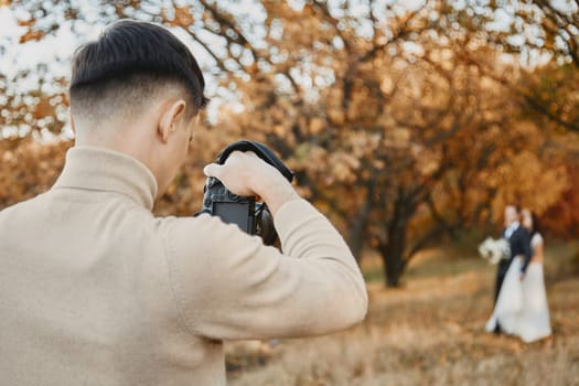 Professional wedding photographer taking pictures of the bride and groom in nature in autumn