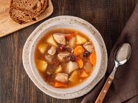 Clear soup with pork, potato, carrot and rosehip. Traditional russian siberian baikal soup yushka with meat. Perfect authentic delicious clear broth soup in rustic style on brown wooden background.